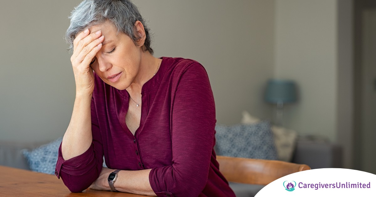 A woman holds her head in her hand, representing the stress that new family caregivers go through.